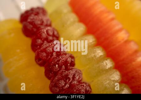 Macro rapprochée de bonbons gélifiés aux couleurs vives disposés en rangées superposées, centre rouge framboise brillant avec des segments gélatineux jaunes, verts et orange Banque D'Images