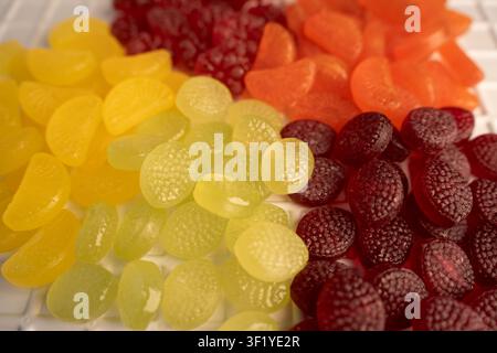 Photographie macro en gros plan de bonbons en gélatine colorés aromatisés aux fruits disposés avec art sur un plateau de table blanc, translucides brillants jaune, orange, rouge Banque D'Images