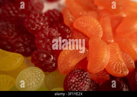 Macro rapprochée de bonbons en gélatine et gomme aromatisés aux fruits assortis et brillants disposés en un tas coloré sur une table, teintes vives orange, rouge, jaune et vert Banque D'Images