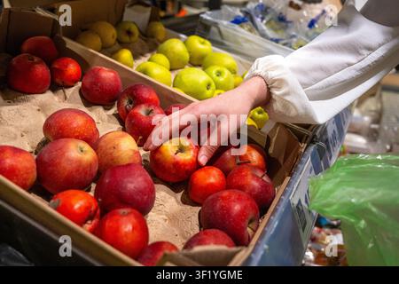 Une personne sélectionnant des pommes fraîches et éclatantes dans un panier de marché entouré d'une variété de couleurs et de textures montrant la beauté des produits de la nature Banque D'Images