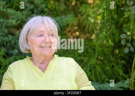 Femme âgée souriante profitant d'un moment de détente en plein air dans le jardin par une journée d'été ensoleillée. Banque D'Images