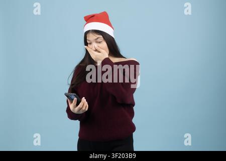 Femme heureuse portant un chapeau de Père Noël tapant sur l'écran de son smartphone affichant des choses positives ... Banque D'Images