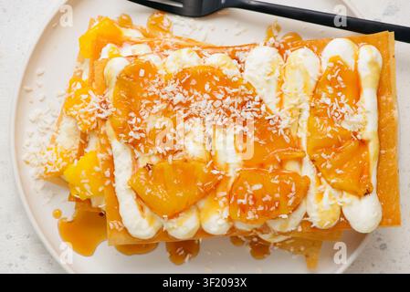 Mille-feuille avec ananas caramélisé, mangue, crème fouettée et noix de coco. Vue de dessus. Mise au point sélective Banque D'Images