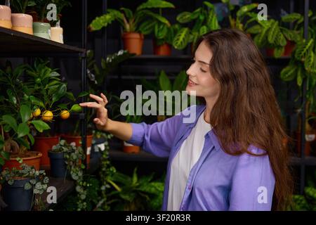 Jeune femme inspectant attentivement un feuillage éclatant autour de nombreux pots de fleurs en terre cuite Banque D'Images