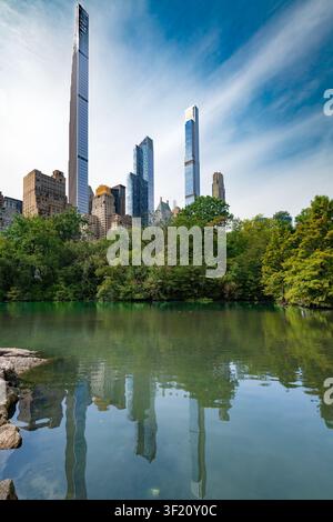 Vue panoramique depuis Central Park montrant les gratte-ciel hauts et élancés de Billionaires Row se reflétant sur la surface calme de The Pond Banque D'Images