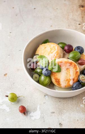 Crêpes au fromage cottage syrniki, beignets à la ricotta avec des fruits rouges frais pour le petit-déjeuner, gros plan sur fond beige Banque D'Images