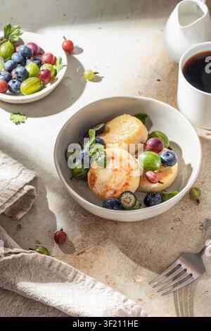 Crêpes au fromage cottage syrniki, beignets de ricotta avec des fruits rouges frais pour le petit-déjeuner sous la lumière vive du matin Banque D'Images