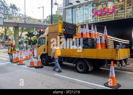Ouvriers municipaux posant des cônes de signalisation orange et blanc sur la chaussée pour délimiter la zone, entretien routier urbain à Hong Kong Banque D'Images