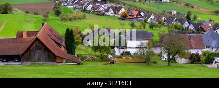 Des collines verdoyantes entourent un charmant village avec des fermes traditionnelles et des toits rouges Banque D'Images