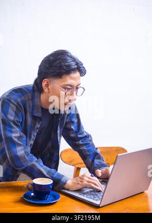 Jeune Asiatique concentré se focalisant sur son ordinateur portable tout en travaillant à distance dans un café, portrait de mode de vie. Banque D'Images