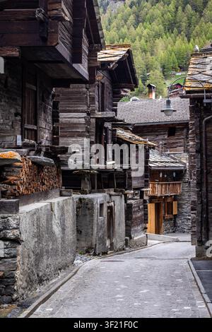 Vue de maisons traditionnelles en bois avec fondations en pierre bordant une étroite rue pavée à Zermatt, Valais, Suisse. Banque D'Images
