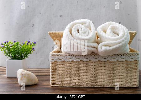Serviettes blanches roulées dans un panier en osier avec décoration d'intérieur sur une table en bois Banque D'Images