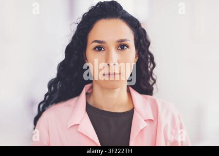 Professionnelle de santé en manteau rose avec une expression sérieuse, cadre clinique, concept de soins de santé Banque D'Images