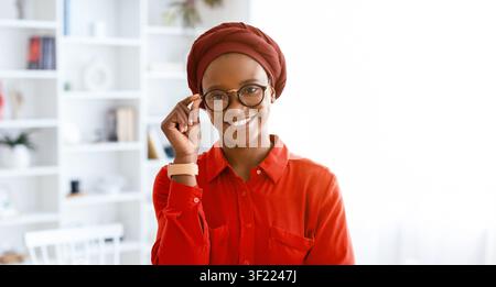 Femme portant des lunettes souriant tout en tenant des verres dans une pièce lumineuse Banque D'Images