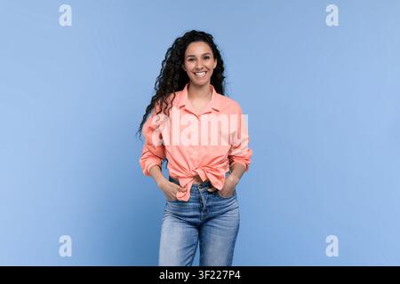 Femme debout devant un fond bleu portant une chemise rose et un jean tout en souriant Banque D'Images