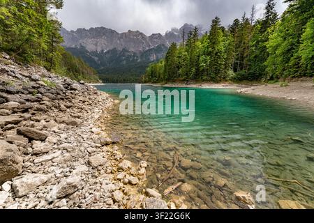 L'eau turquoise vive du lac d'Eibsee est encadrée par une rive rocheuse et des forêts de pins denses en Bavière, Allemagne. Les sommets escarpés du Wetterst Banque D'Images
