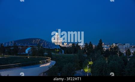 Vue nocturne du parc Zaryadye avec dôme de verre moderne et bâtiment illuminé de l'Université d'État de Moscou. Paysage urbain sous un ciel bleu profond. Banque D'Images