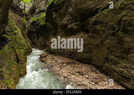La rivière Partnach aux eaux rapides dévale les parois étroites et moussues en pierre de la gorge de Partnachklamm en Bavière, Allemagne. De profondes falaises rocheuses s'élèvent Banque D'Images