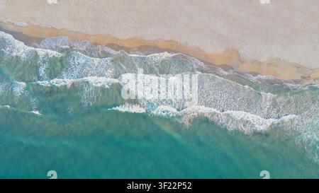 Vue aérienne horizontale par le dessus des vagues turquoise de l'océan déferlant sur une plage de sable avec une écume blanche étincelante par une journée d'été ensoleillée pour Banque D'Images