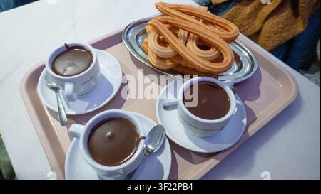 Churros accompagnés de trois tasses de riche chocolat chaud servis sur un plateau rose clair Banque D'Images