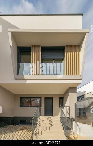 Maison moderne à deux étages dotée d'un balcon surplombant avec lattes en bois, rampes en verre et escaliers menant à l'entrée principale. Banque D'Images