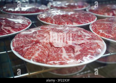 Tranches de bœuf cru fraîches avec une belle marbrure enveloppées dans du plastique sur des assiettes dans une vitrine de restaurant boucher. Banque D'Images