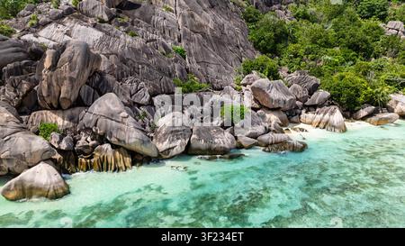Formations de granit le long de la côte avec des eaux turquoise et une végétation tropicale luxuriante. Seychelles, La Digue. Banque D'Images