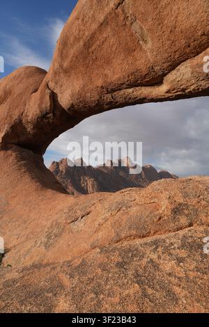 L'arc naturel en granit de Spitzkoppe encadre les sommets montagneux accidentés de la région d'Erongo en Namibie. Banque D'Images