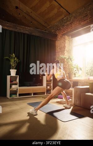 Femme effectuant une fente latérale avec poids lors d'un entraînement à domicile. Banque D'Images