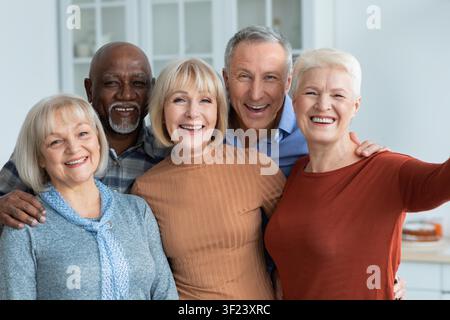 Amis seniors multiraciaux heureux souriant ensemble dans une cuisine moderne, portrait de groupe Banque D'Images