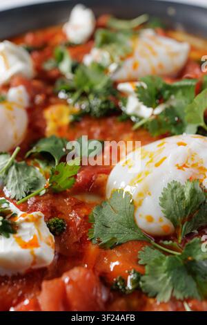 Un plat vibrant de shakshuka mettant en vedette des œufs pochés nichés dans une sauce tomate épicée, garni d'herbes fraîches pour une option savoureuse pour le petit-déjeuner ou le brunch Banque D'Images