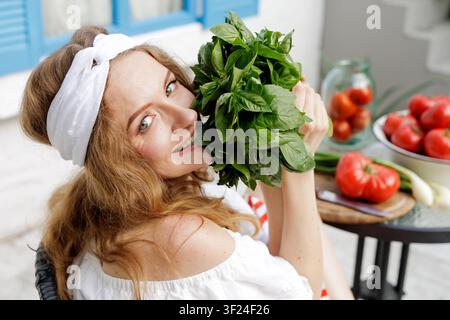 Une femme joyeuse tient une poignée de basilic frais, entourée de tomates mûres, représentant la joie de cuisiner avec des ingrédients frais. Banque D'Images