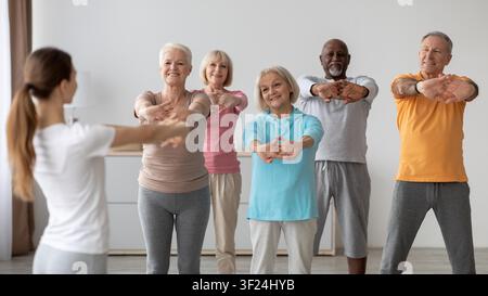 Groupe caucasien âgé heureux participant à un cours d'étirement, activité d'exercice en intérieur Banque D'Images