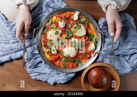 Un plat de shakshuka vibrant mettant en vedette des œufs pochés, des herbes fraîches et une sauce tomate riche, parfait pour le brunch ou un repas cosy. Banque D'Images