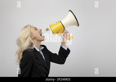 Femme confiante hurlant à travers un mégaphone en costume d'affaires, fond de bureau, concept d'autonomisation Banque D'Images