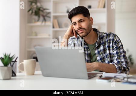Jeune homme concentré en chemise à carreaux travaillant sur un ordinateur portable au bureau à domicile, concept commercial Banque D'Images