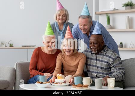 Groupe caucasien de personnes âgées heureuses célébrant un anniversaire avec un gâteau, souriant ensemble à l'intérieur Banque D'Images