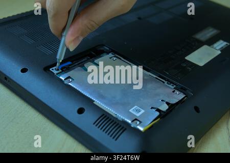 Gros plan de la main d'un technicien utilisant un tournevis métallique pour dévisser le support ou le caddy du disque interne d'un châssis d'ordinateur portable noir. Mise au point sur le bricolage technique Banque D'Images