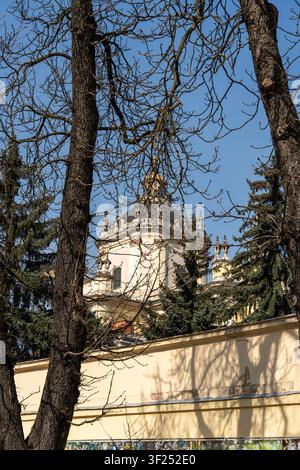 Un bâtiment historique avec un dôme dépasse à travers les branches des grands arbres dans un parc de la ville. Le soleil brille sur la structure, révélant des détails et des couleurs Banque D'Images