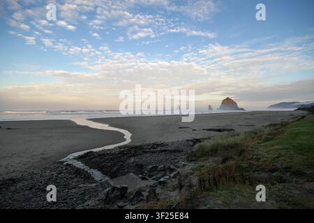 Paysage côtier étendu de Cannon Beach, Oregon, avec Haystack Rock et des falaises sous un ciel matinal dramatique et une marée descendante. Banque D'Images