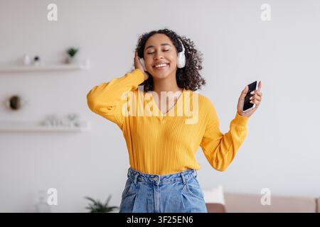 Jeune femme noire heureuse écoutant de la musique avec des écouteurs à la maison, concept de mode de vie Banque D'Images