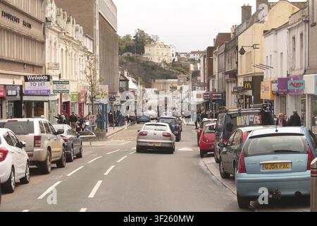 Une rue urbaine animée de voitures et de piétons, bordée d'une variété de magasins sous un ciel nuageux, Torquay, Devon, Royaume-Uni Banque D'Images