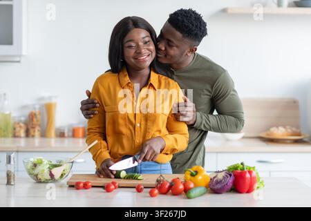 Couple cuisinant ensemble dans la cuisine, femme afro-américaine coupant des légumes, moment heureux Banque D'Images