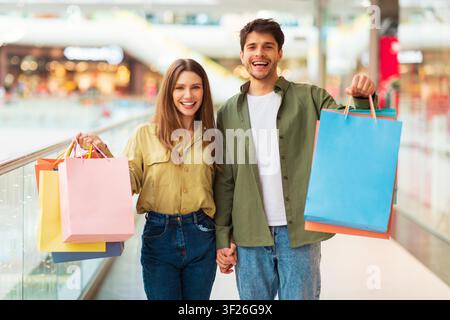 Jeun couple heureux tenant ensemble des sacs de shopping colorés dans un centre commercial, concept de vente au détail Banque D'Images