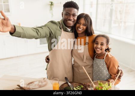 Famille afro-américaine heureuse cuisinant ensemble dans la cuisine, préparant une salade saine et des smoothies Banque D'Images