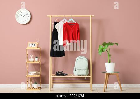 Uniforme scolaire et sac à dos sur un portant à vêtements en bois avec une horloge et une plante dans une pièce moderne Banque D'Images