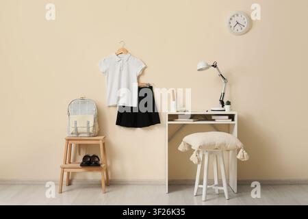 Uniforme scolaire avec sac à dos et chaussures Mary Jane à côté d'un bureau d'étude avec lampe et horloge sur un mur beige, uniforme scolaire composé d'un polo blanc s Banque D'Images