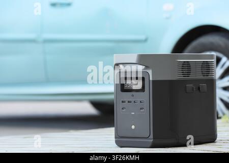 Station d'alimentation portable avec affichage numérique et plusieurs ports pour le chargement extérieur à côté d'une voiture, cette solution énergétique moderne fournit une électricité de secours Banque D'Images