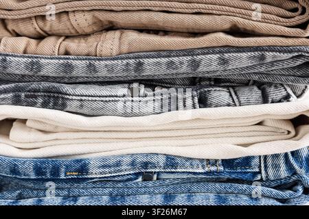 Pile de jeans en denim pliés et de pantalons en coton de diverses couleurs, vue rapprochée de la texture des vêtements décontractés Banque D'Images