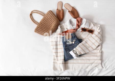 Tenue d'été décontractée pour femme avec sac en paille, jeans en denim, pull rayé et accessoires sur fond blanc Banque D'Images